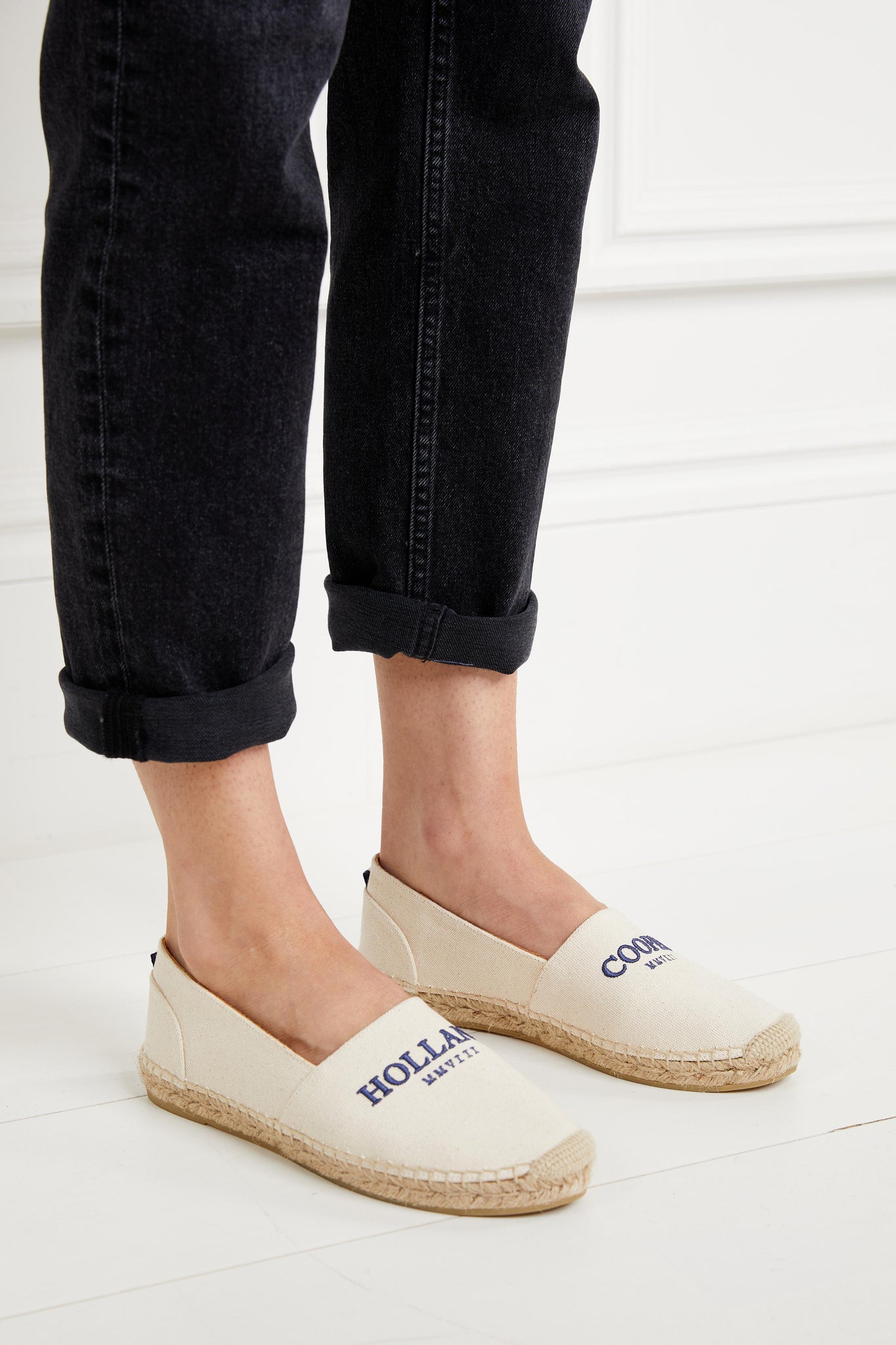 classic style natural canvas espadrille with plaited jute sole and jute toe cap with navy embroidered branding on top, paired with rolled up black slim jeans