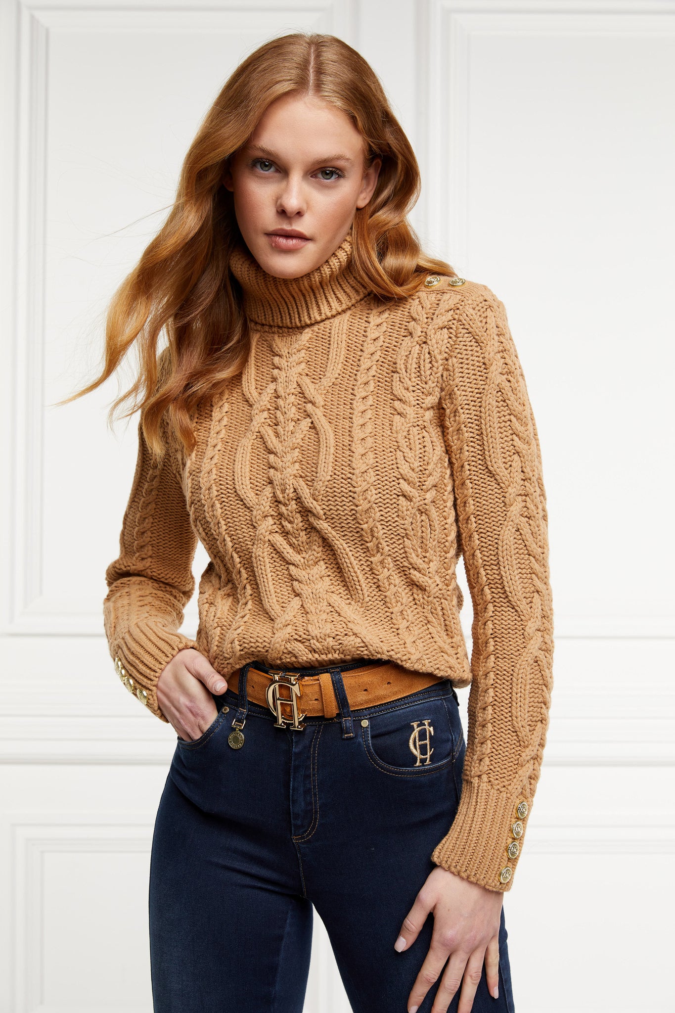 a chunky cable knit roll neck jumper in camel with dropped shoulders and thick ribbed cable trims and gold buttons on cuffs and collar