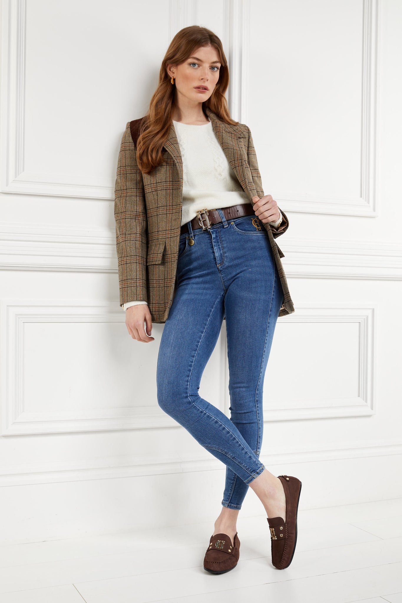 Classic brown suede loafers with a leather sole and top stitching details and gold hardware paired with skinny denim jeans, brown belt, cream crew neck knit and bredon tweed blazer