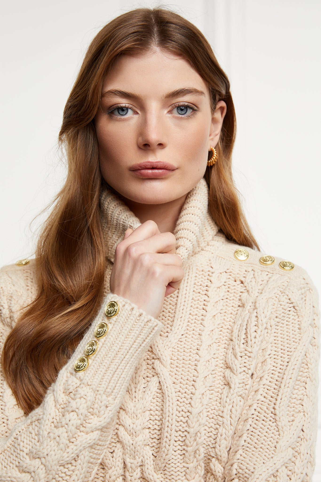 a chunky cable knit roll neck jumper in oatmeal with dropped shoulders and thick ribbed cable trims and gold buttons on cuffs and collar