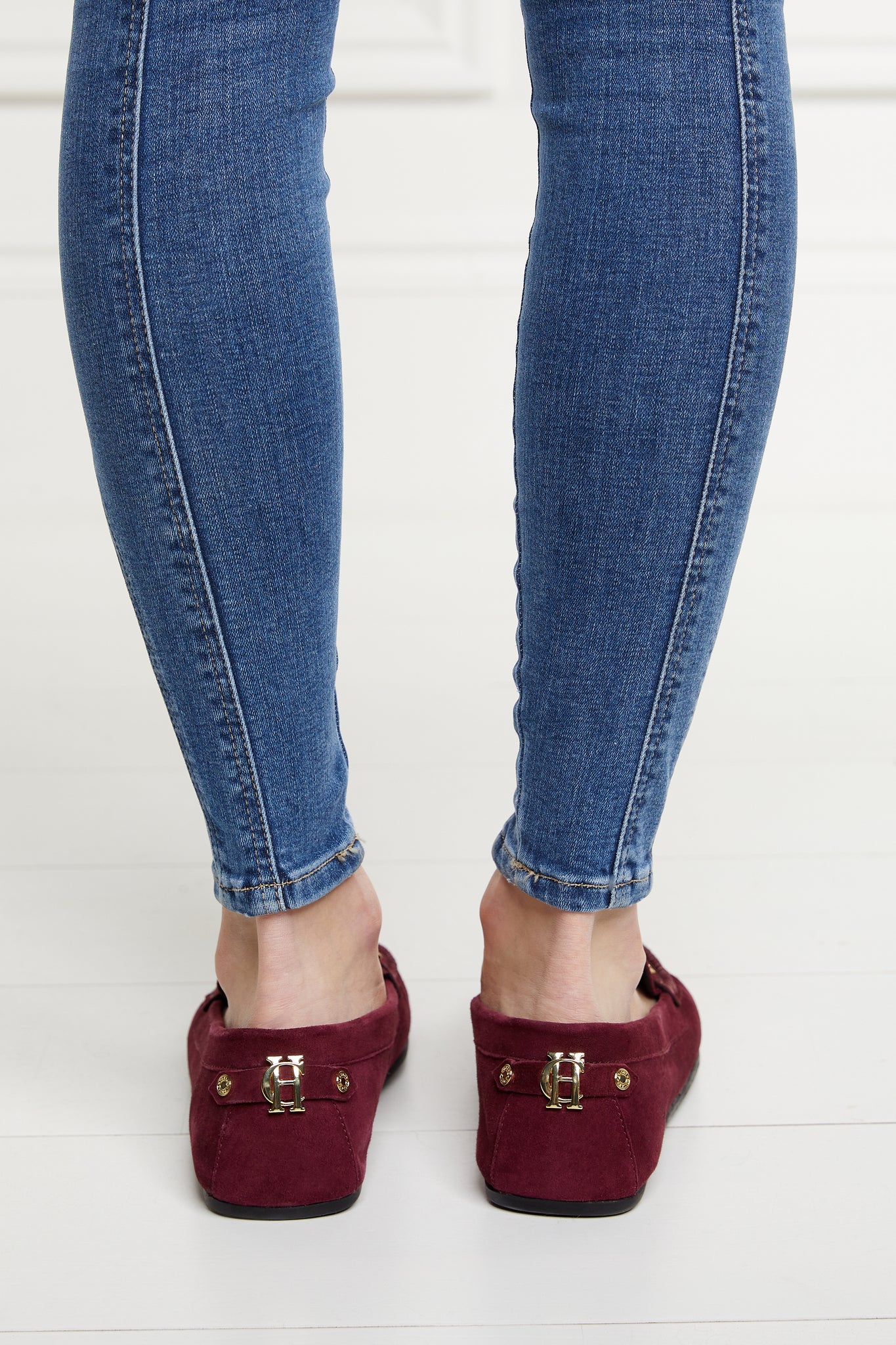 Back of classic deep red suede loafers with a leather sole and gold hardware paired with skinny denim jeans