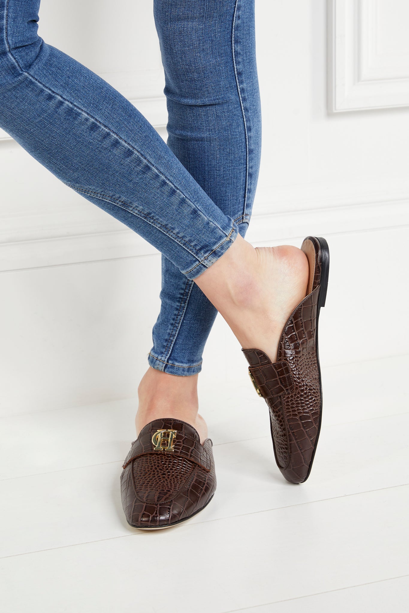 Brown croc embossed leather backless loafers with a slightly pointed toe and gold hardware to the top paired with denim skinny jeans