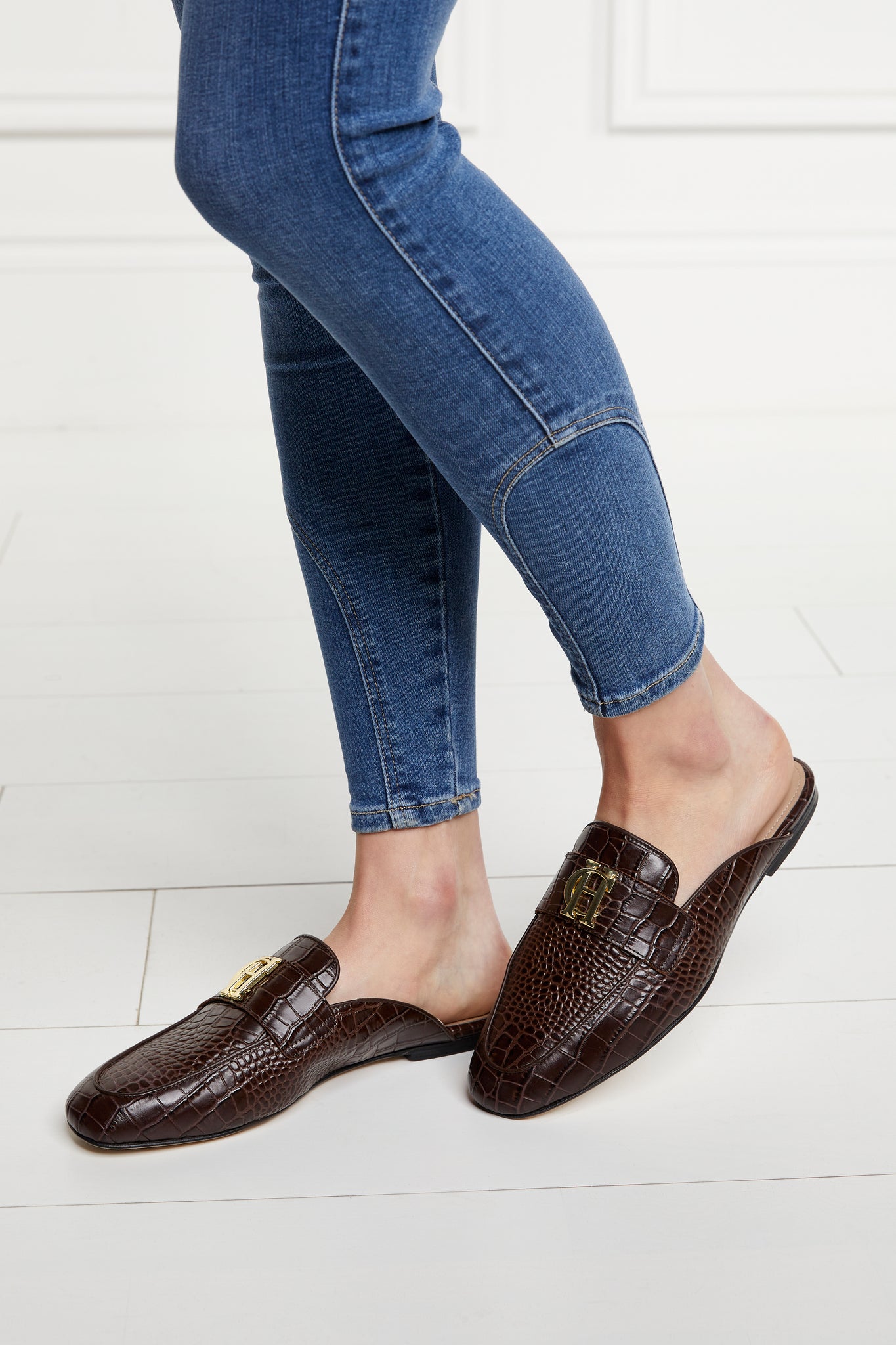Brown croc embossed leather backless loafers with a slightly pointed toe and gold hardware to the top paired with denim skinny jeans