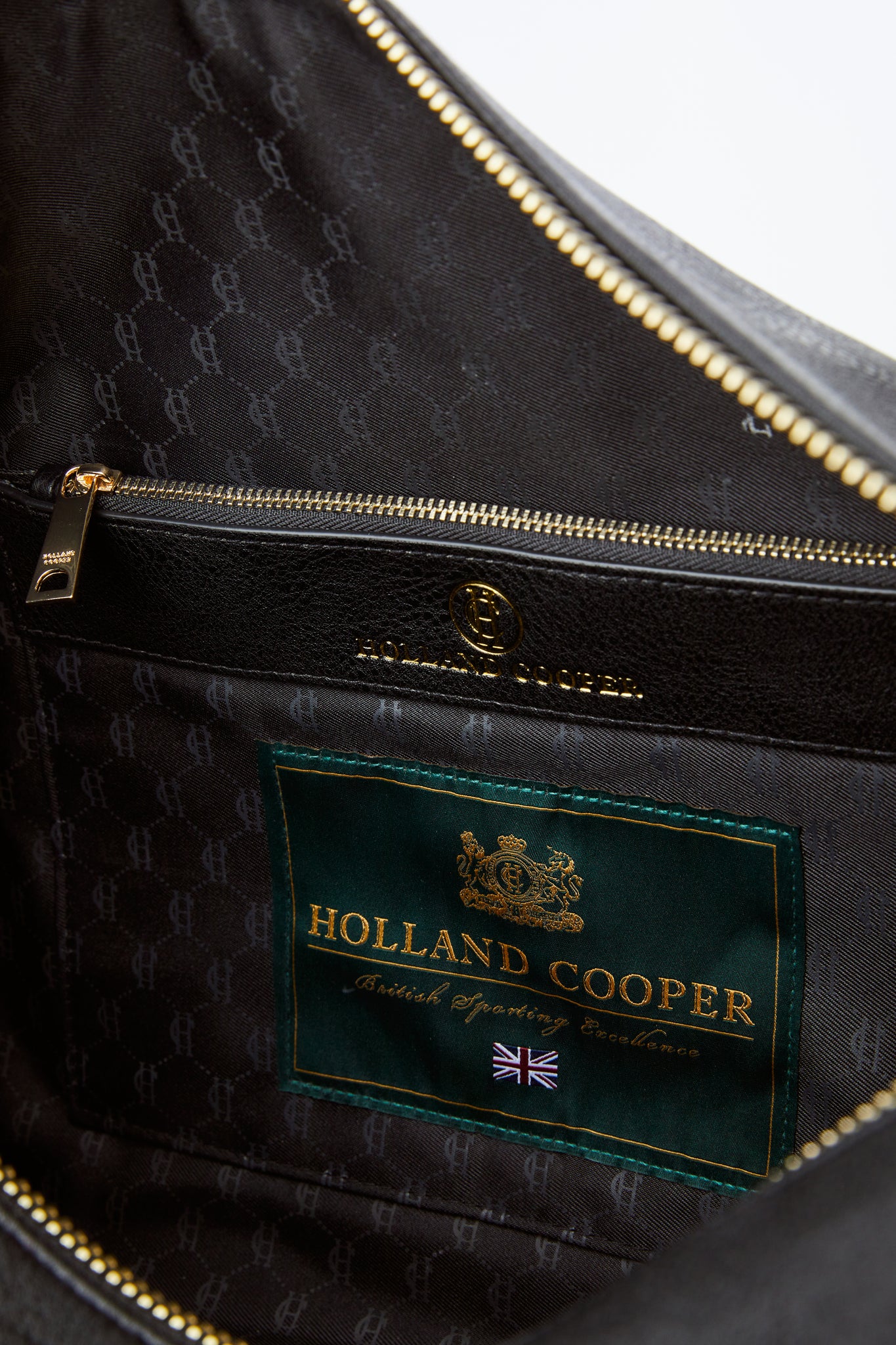 close up of inside of black faux leather travel holdall showing zip pouch and black monogram lining 