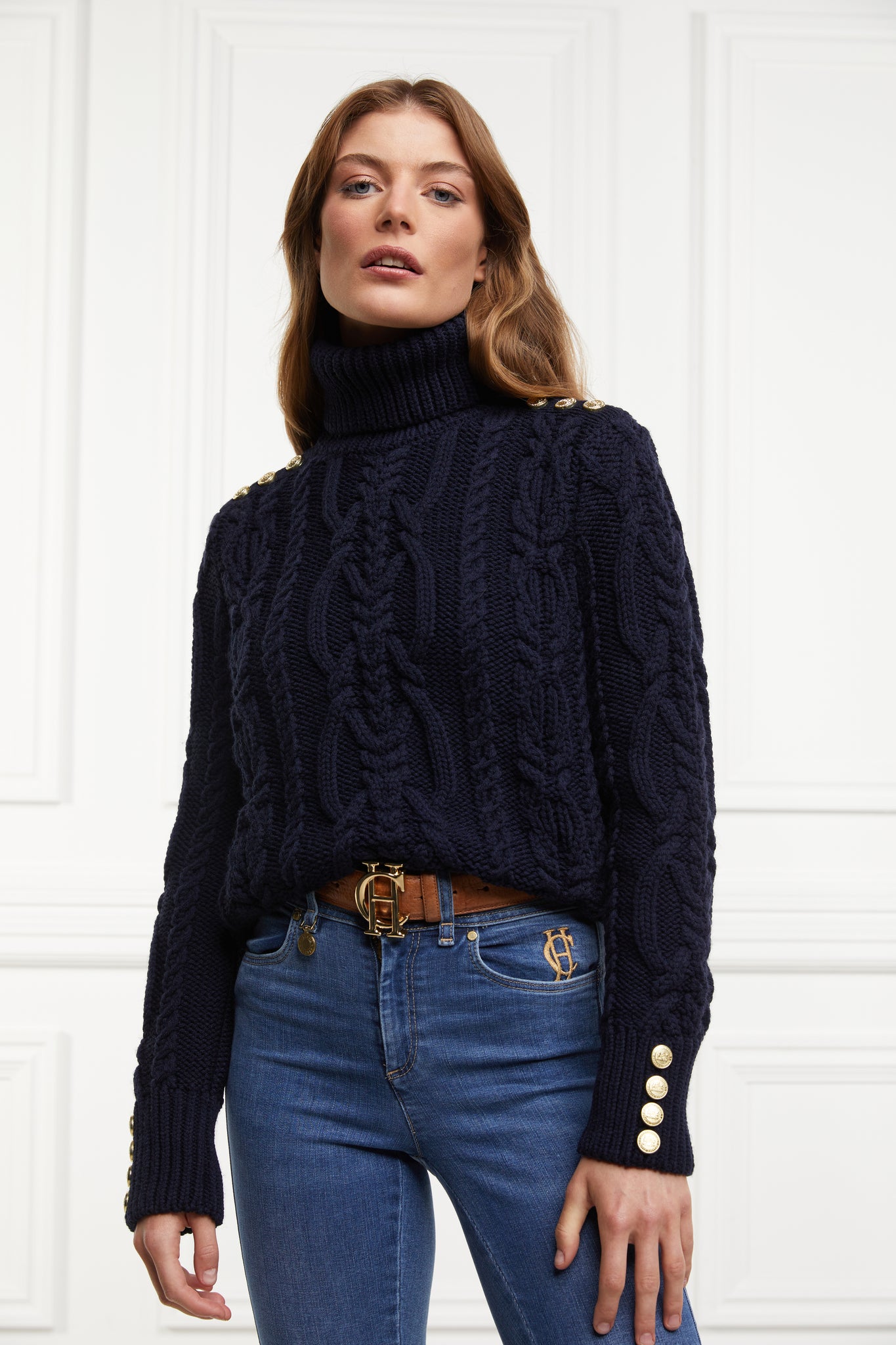 a chunky cable knit roll neck jumper in navy with dropped shoulders and thick ribbed cable trims and gold buttons on cuffs and collar