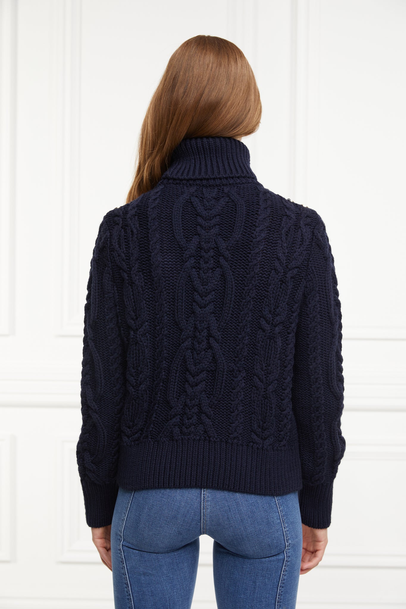 a chunky cable knit roll neck jumper in navy with dropped shoulders and thick ribbed cable trims and gold buttons on cuffs and collar