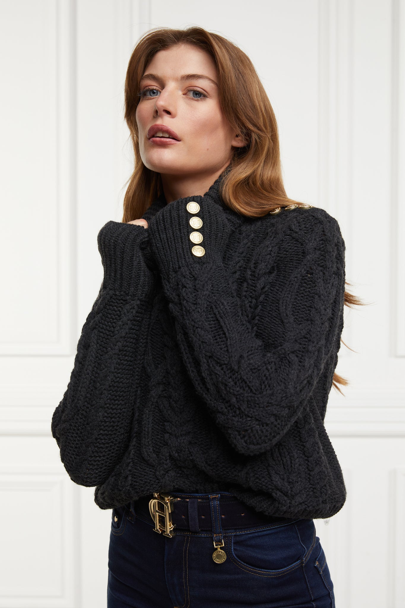 a chunky cable knit roll neck jumper in dark grey with dropped shoulders and thick ribbed cable trims and gold buttons on cuffs and collar