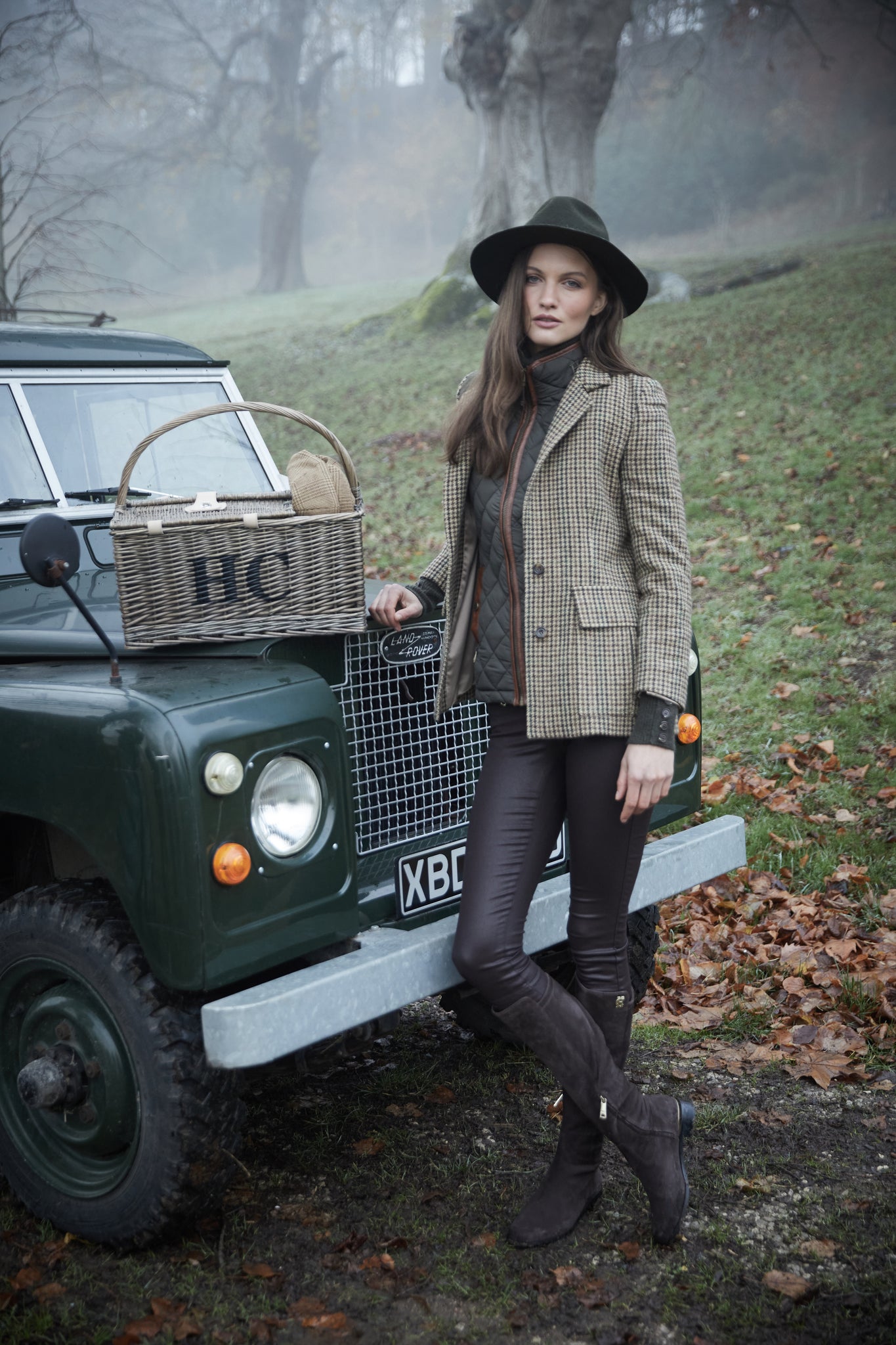womens classic slim fit single breasted blazer in green tan and brown houndstooth tweed with lower patch pockets with concealed button flap contrast khaki suede shoulder gun patch with elbow patches and horn button finish on cuffs and front worn with diamond quilt khaki gilet chocolate wet look trousers and chocolate knee high boots 