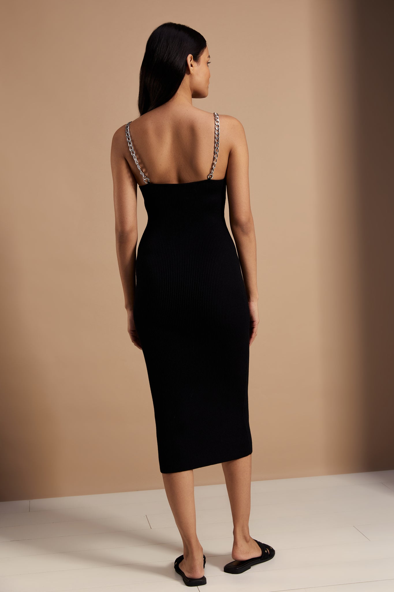back shot of womens ribbed black v neck midi dress with silver chain straps and black suede sliders
