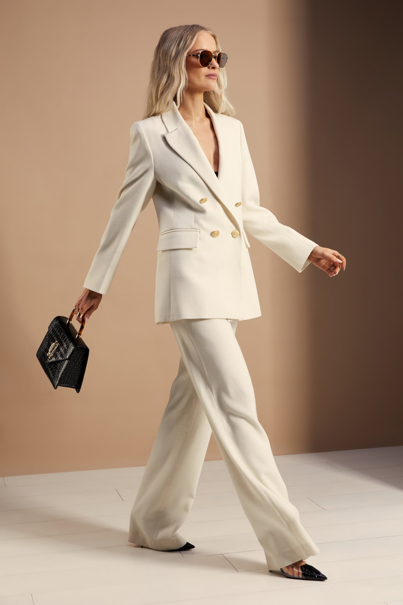 longline double breasted wool blazer in ivory tailor made in britain with relaxed fit welt pockets and gold buttons on the front and cuffs worn with tailored trousers in the same colour 