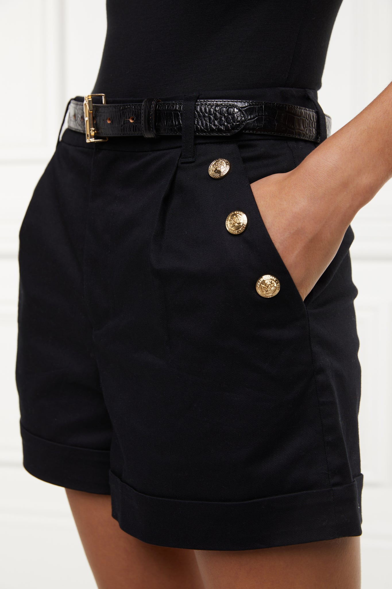 gold rivet on pocket detail of womens black high rise tailored shorts with decorative gold rivets that follow the pocket line in a sailor style with a turned up hem worn with black bodysuit