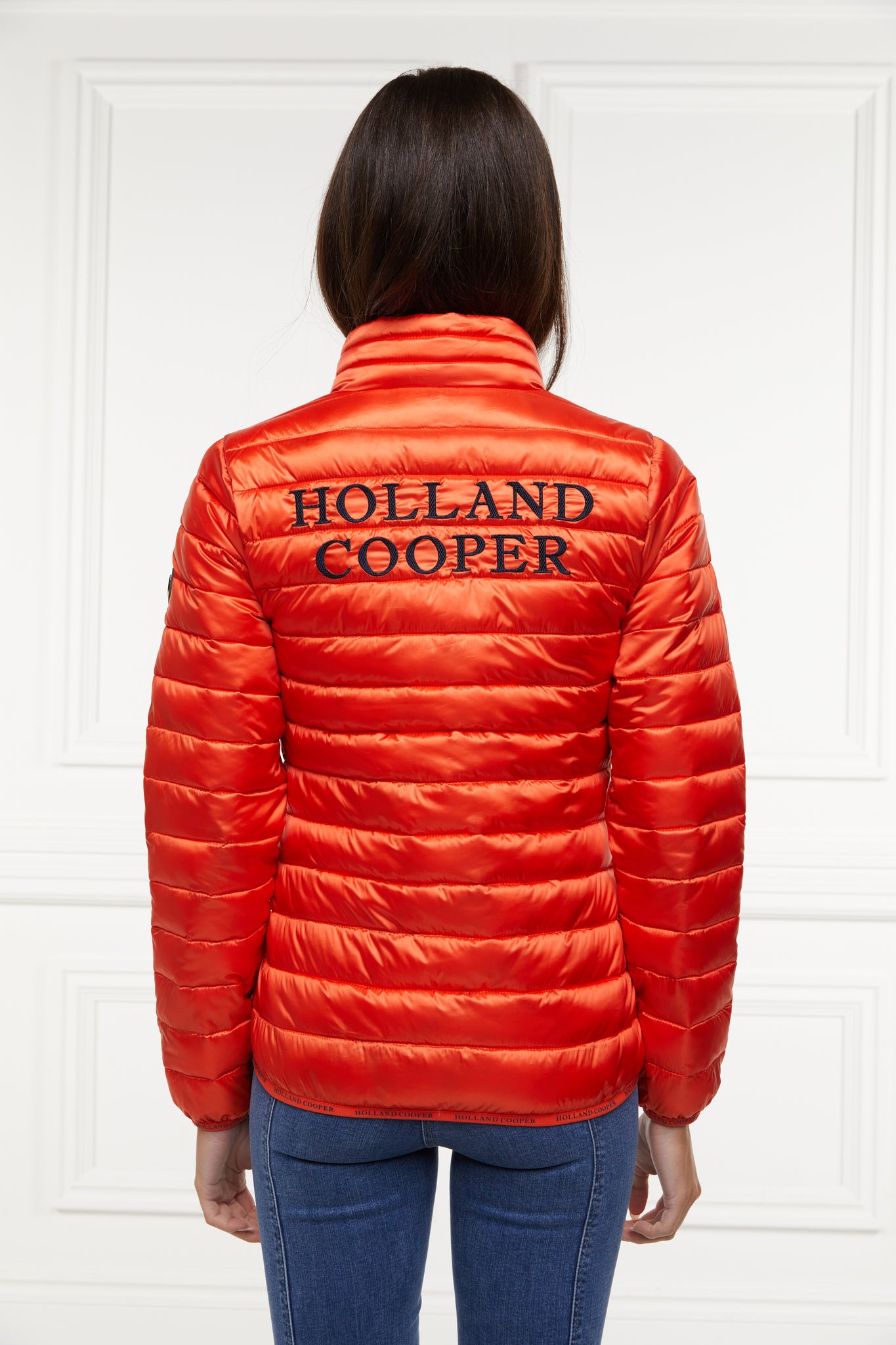 back of womens lightweight hoodless padded orange jacket with embroidery detail on back high neck and elasticated cuffs and hem. easily packs away into separate small bag of the same colour with handle 