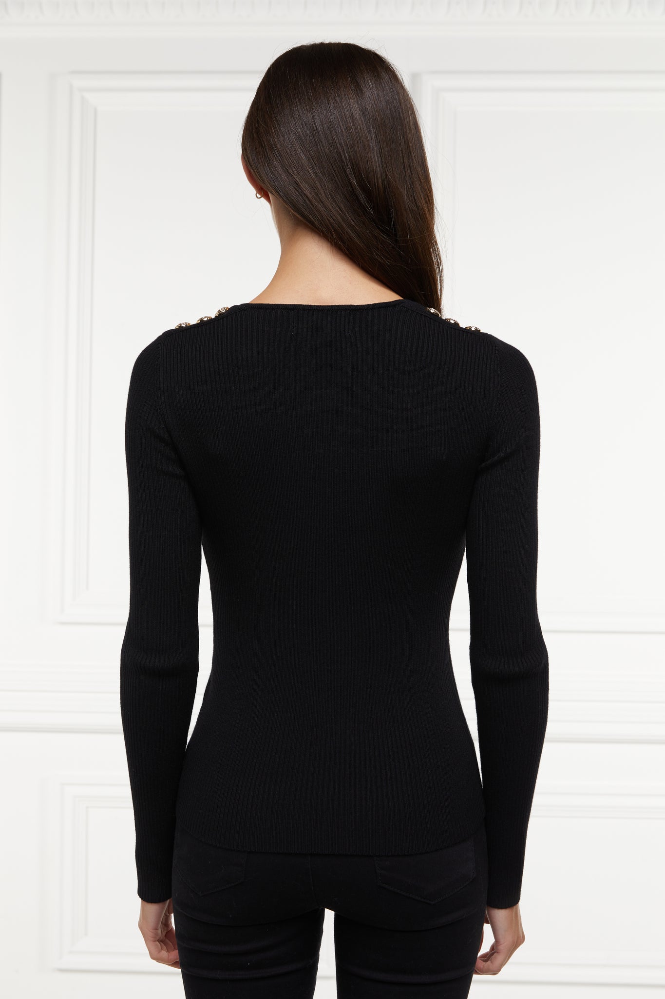 back of a form fitting finely ribbed long sleeved knitted top in black with a sweetheart neckline and gold buttons on shoulders