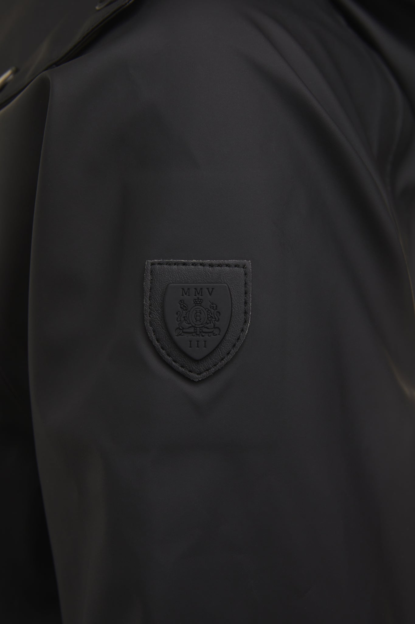 shield detail of womens black hooded rain coat with black hardware 