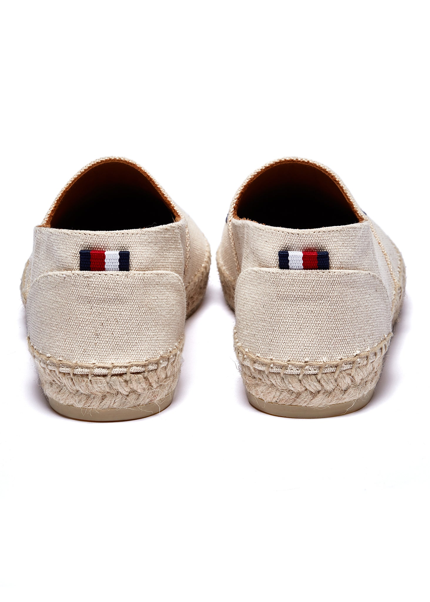 Back of classic style natural canvas espadrille with plaited jute sole and jute toe cap with navy embroidered branding on top and a red, white and blue small tag on the heel