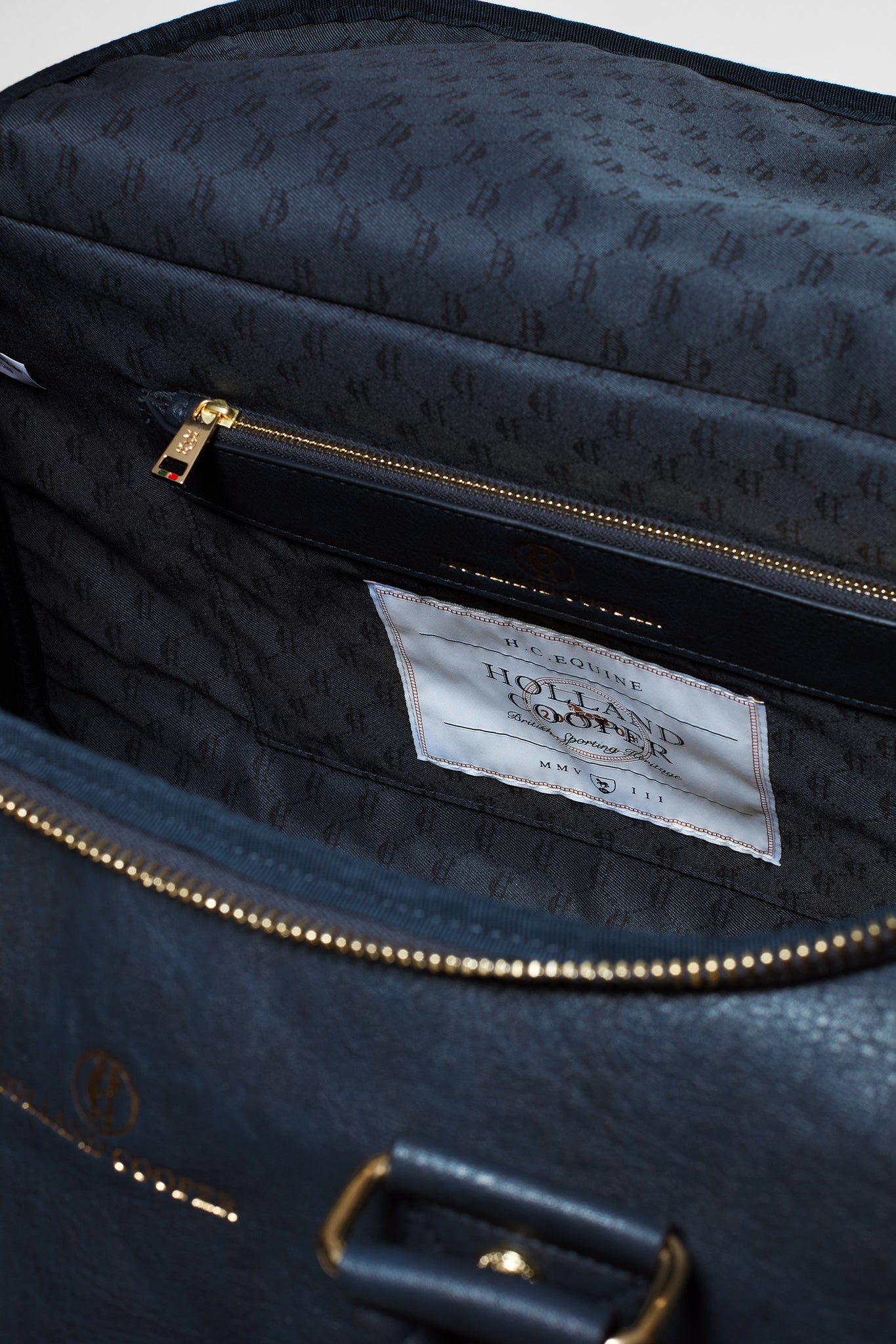 inside of navy faux leather holdall bag showing navy monogram print lining and internal zip pocket
