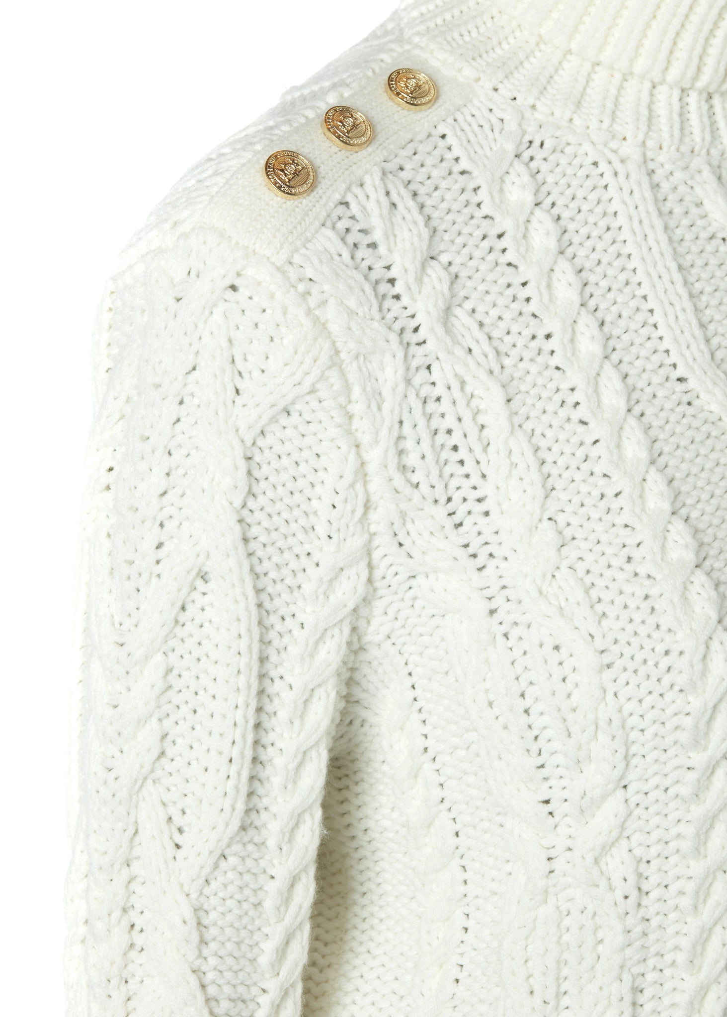gold button detail across shoulder of a chunky cable knit roll neck jumper in cream with dropped shoulders and thick ribbed cable trims and gold buttons on cuffs and collar