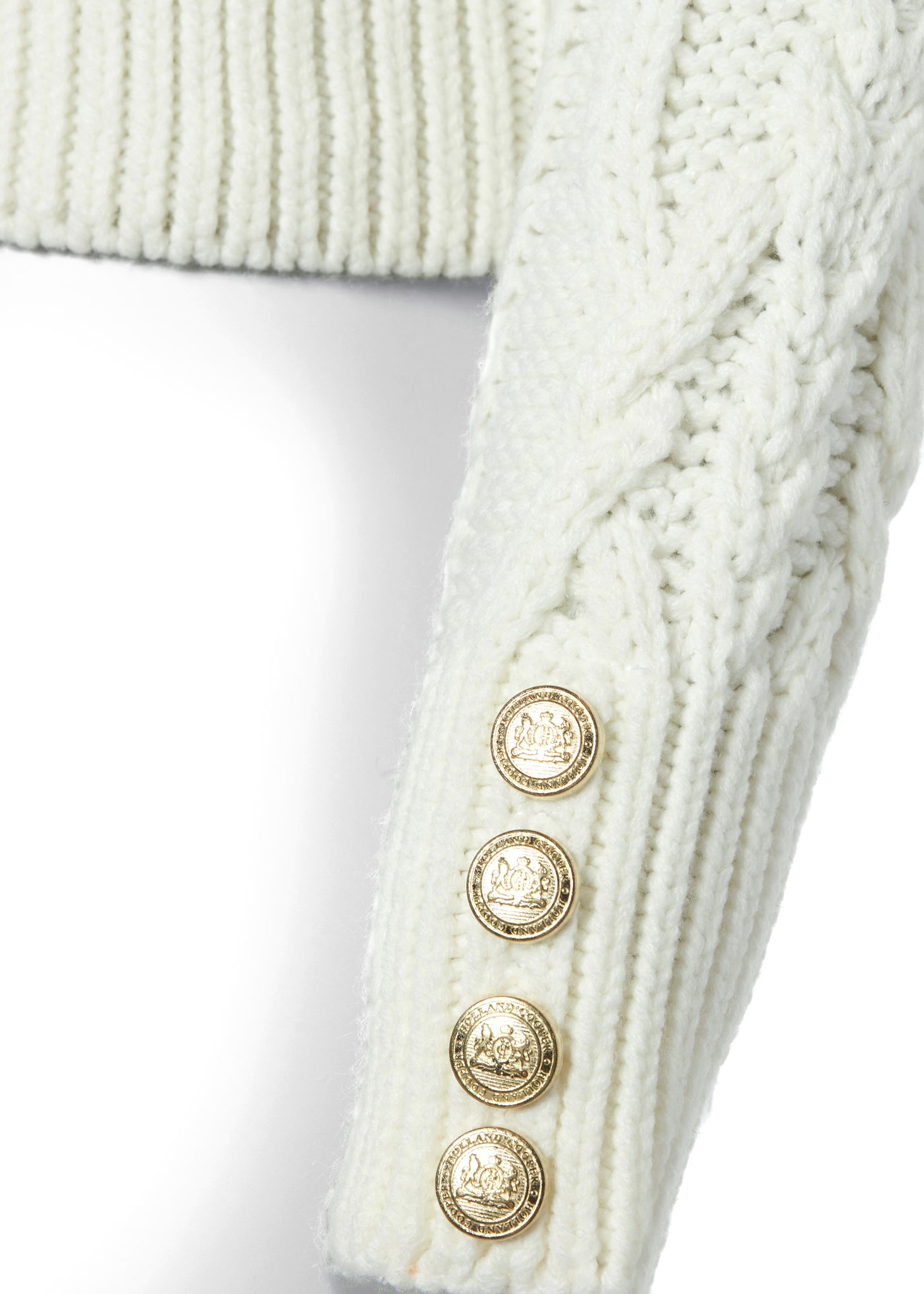 gold button detail on cuffs of a chunky cable knit roll neck jumper in cream with dropped shoulders and thick ribbed cable trims and gold buttons on cuffs and collar