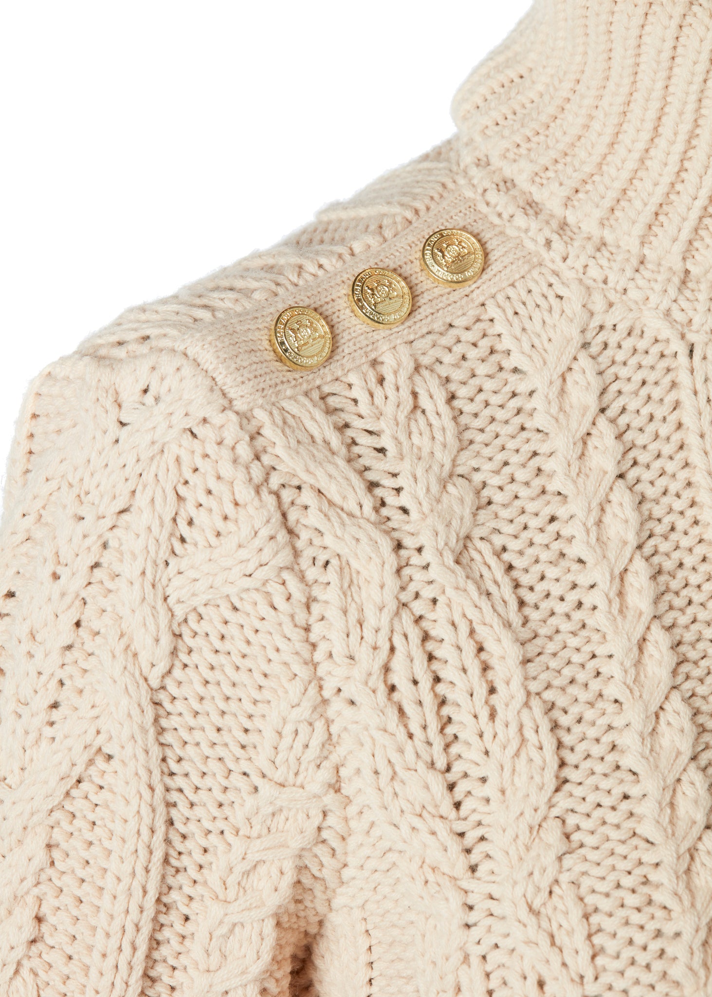 gold button detail accross shoulder of a chunky cable knit roll neck jumper in oatmeal with dropped shoulders and thick ribbed cable trims and gold buttons on cuffs and collar