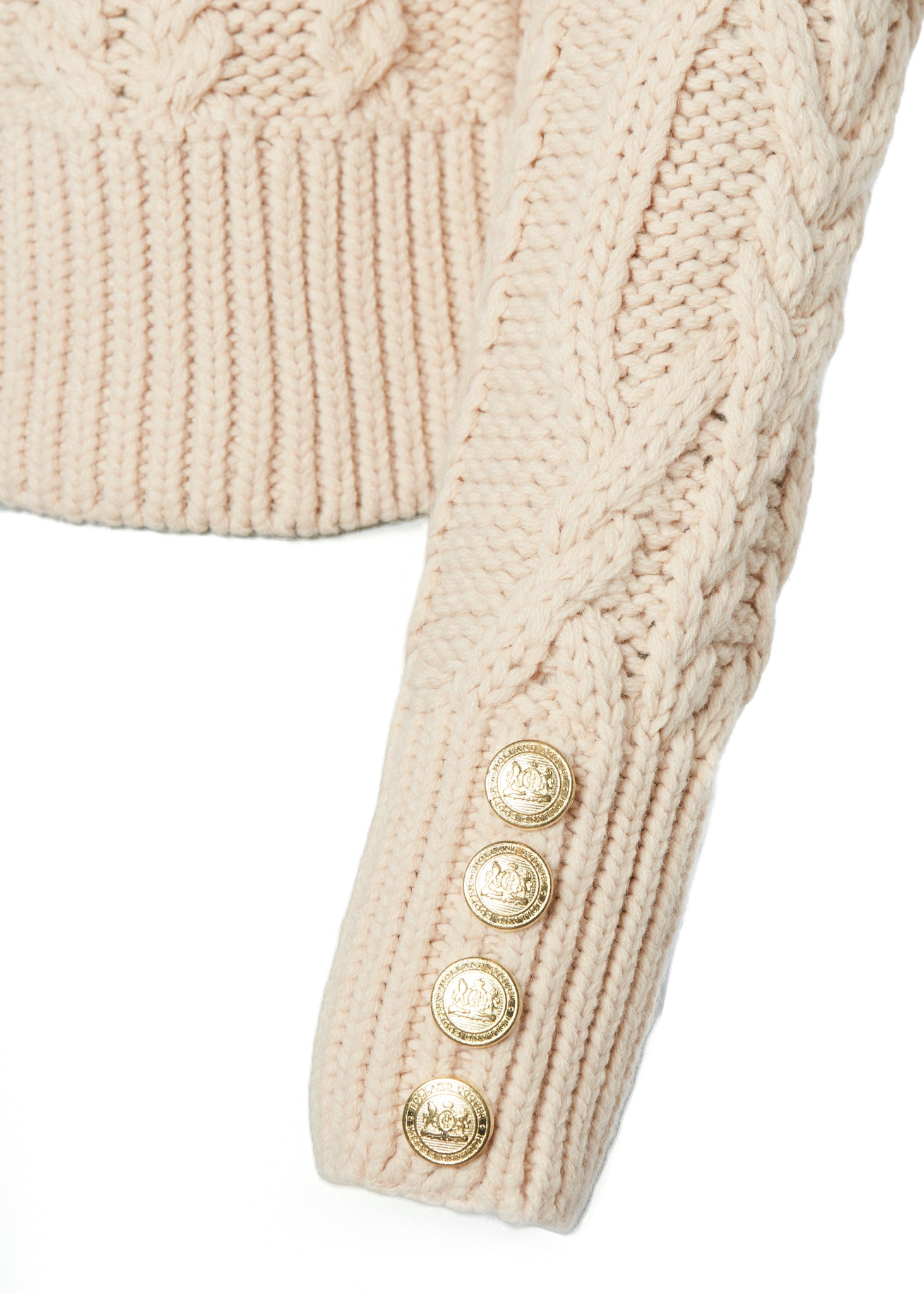 gold button detail on the cuffs of a chunky cable knit roll neck jumper in oatmeal with dropped shoulders and thick ribbed cable trims and gold buttons on cuffs and collar