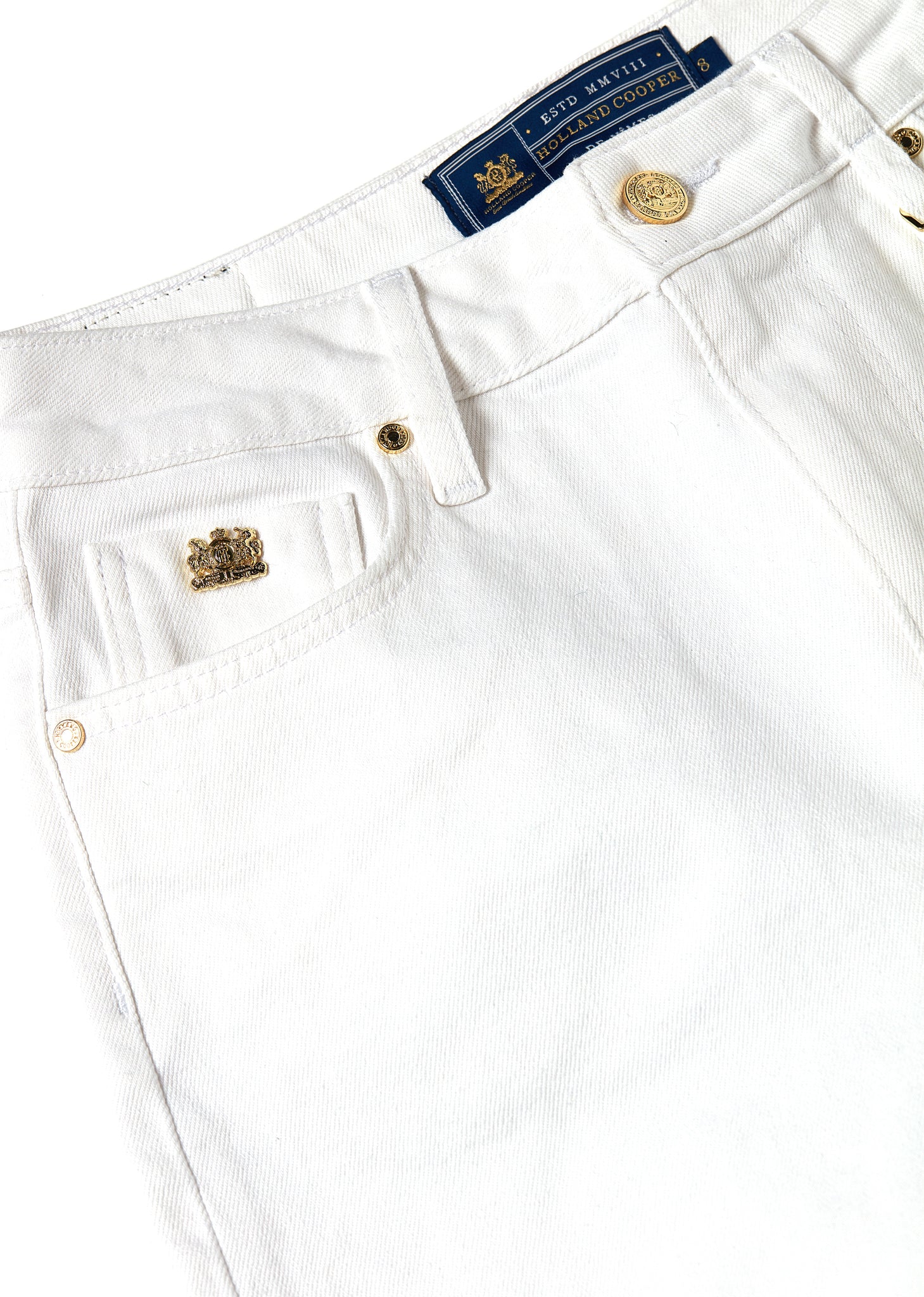 front pocket detail of womens white high waisted denim shorts with raw edge hemline and two open front pockets and two open back pockets with gold hc crest rivet in right front pocket
