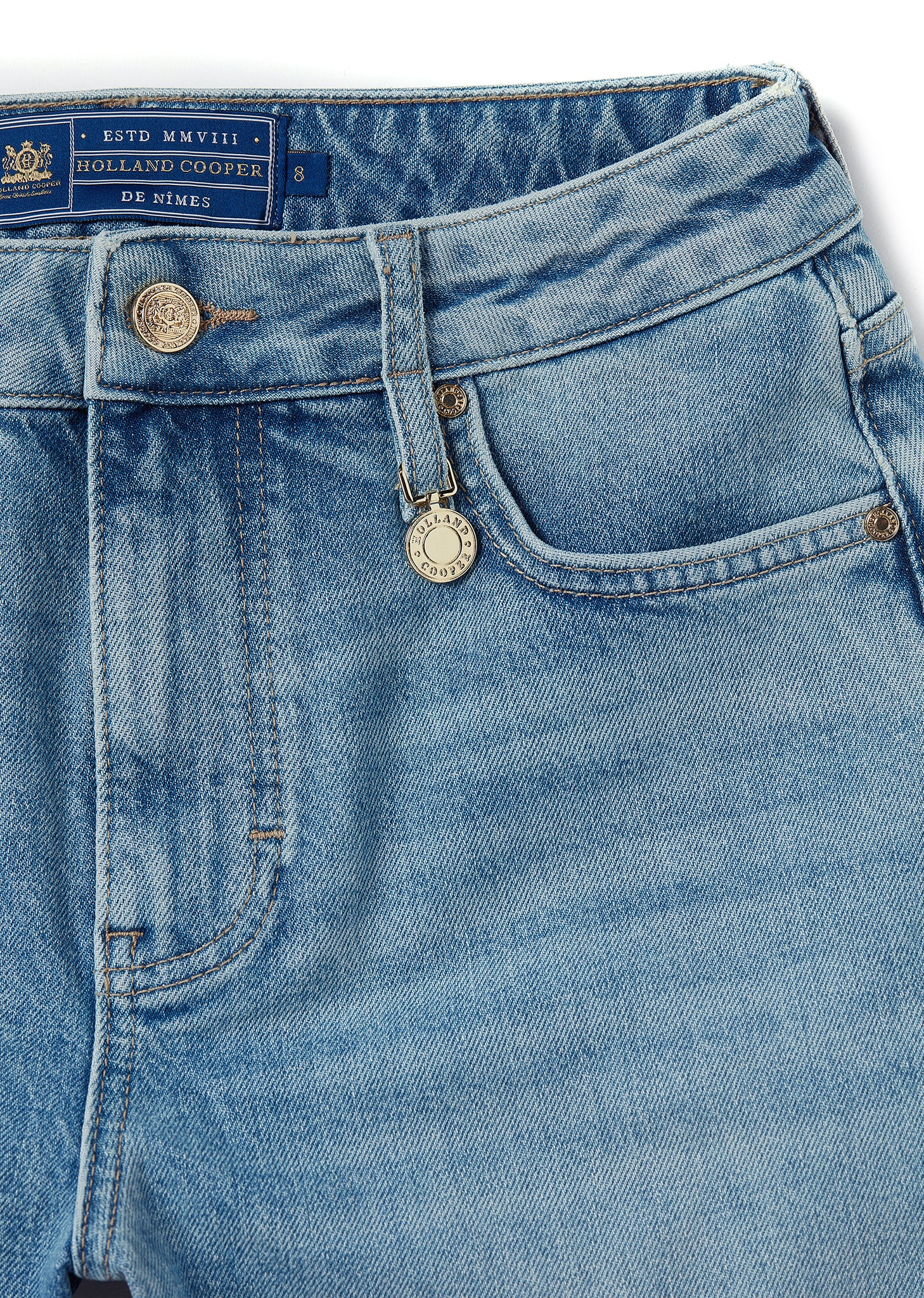front pocket detail of womens blue denim shorts with raw edge hemline and two open front pockets and two open back pockets with gold hc crest rivet in right front pocket