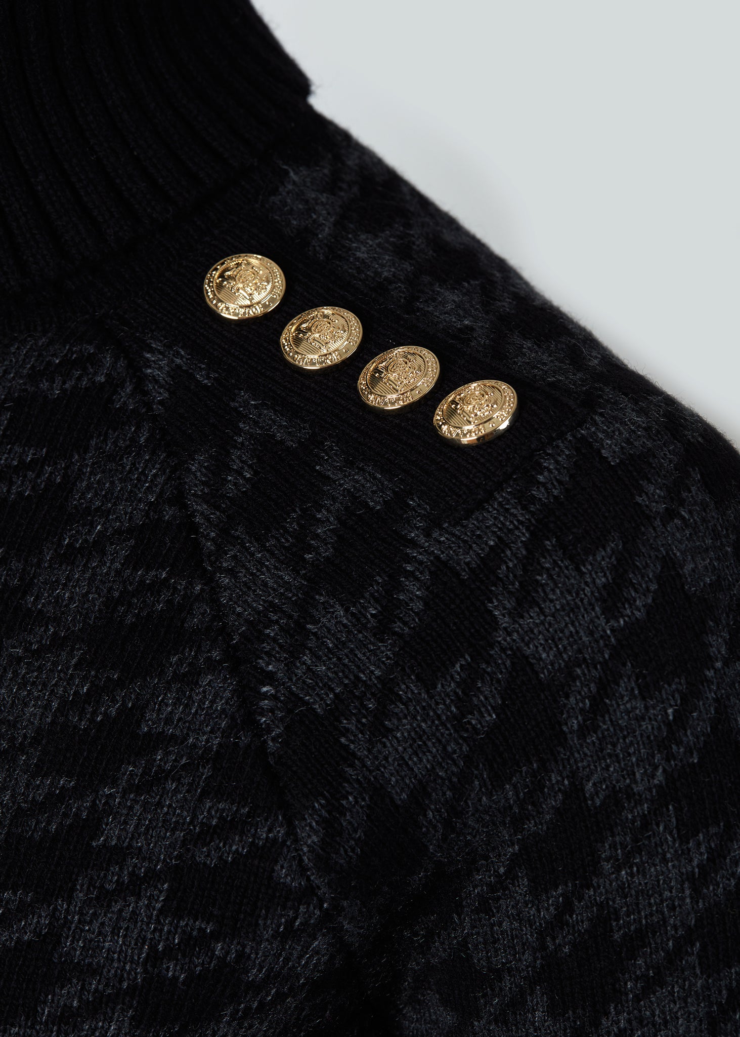 gold button detail across shoulders of a classic black and grey houndstooth jumper with contrast black cuffs, roll neck and split ribbed hem with gold button detail on the cuffs and collar
