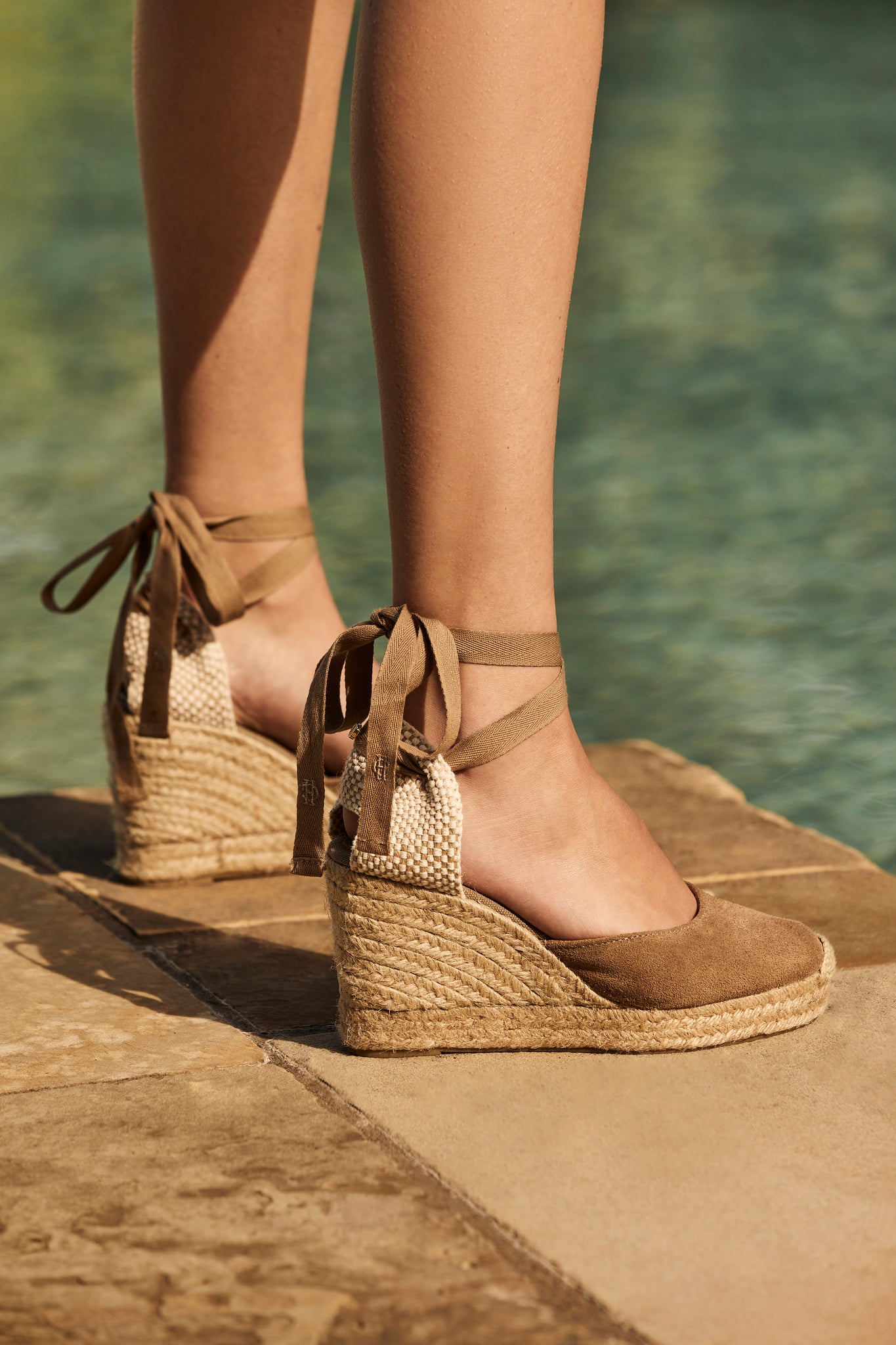 4 inch braided jute wedge heel with taupe suede top and tie up taupe ribbons around the ankle worn standing by the edge of a pool