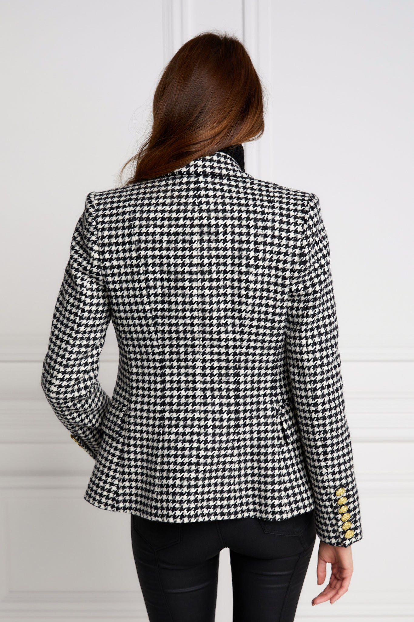 back of British made double breasted blazer that fastens with a single button hole to create a more form fitting silhouette with two pockets and gold button detailing this blazer in black and white houndstooth