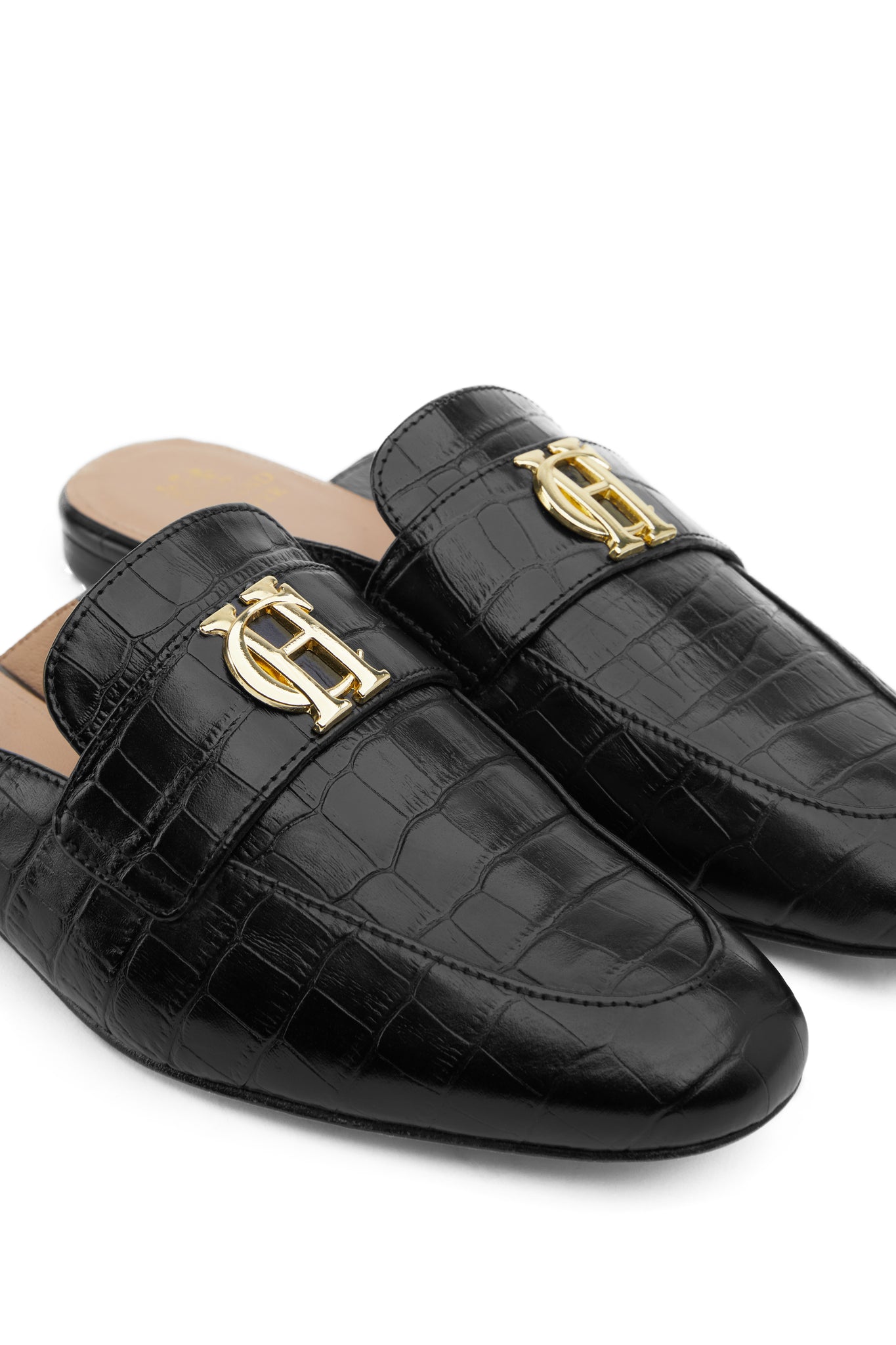 Close up detail shot of Black croc embossed leather backless loafers with a slightly pointed toe and gold hardware to the top
