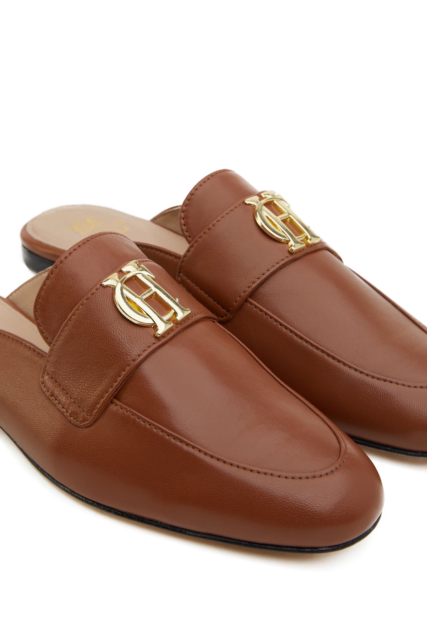 Close up of gold hardware on tan leather backless loafers with a slightly pointed toe