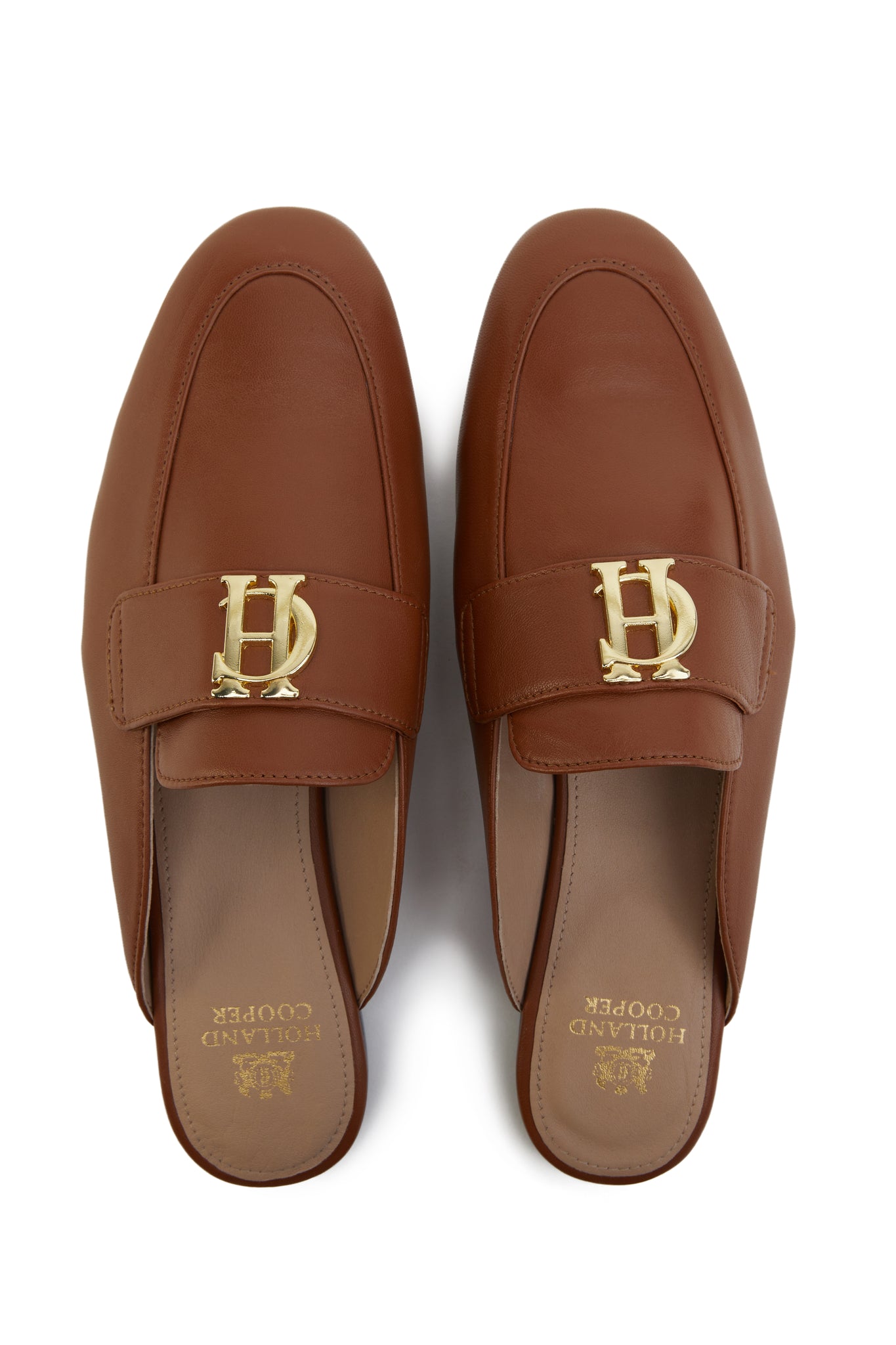 Birds eye view of tan leather backless loafers with a slightly pointed toe and gold hardware to the top and gold foil branding to inner sole