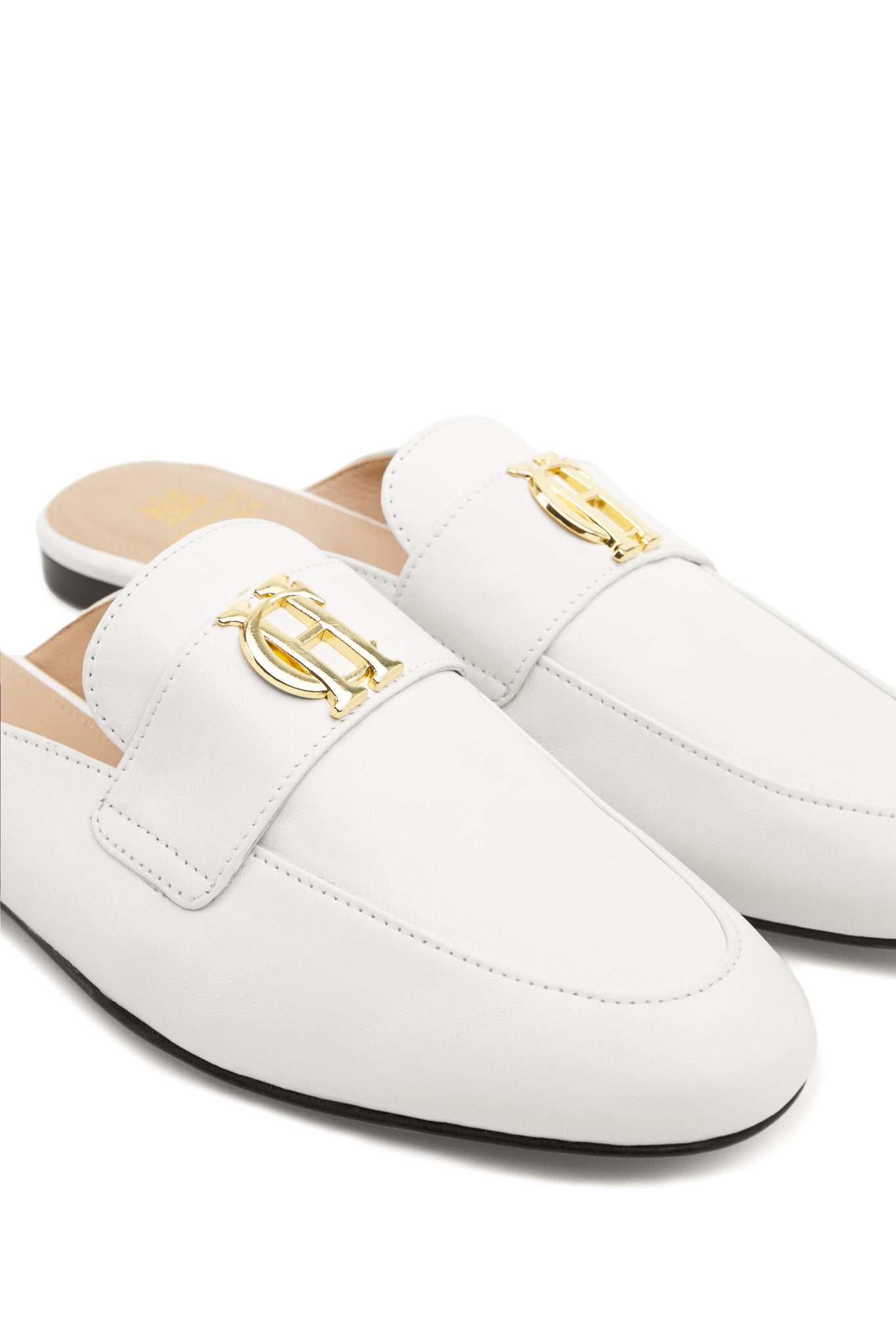 Close up of gold hardware on white leather backless loafers with a slightly pointed toe