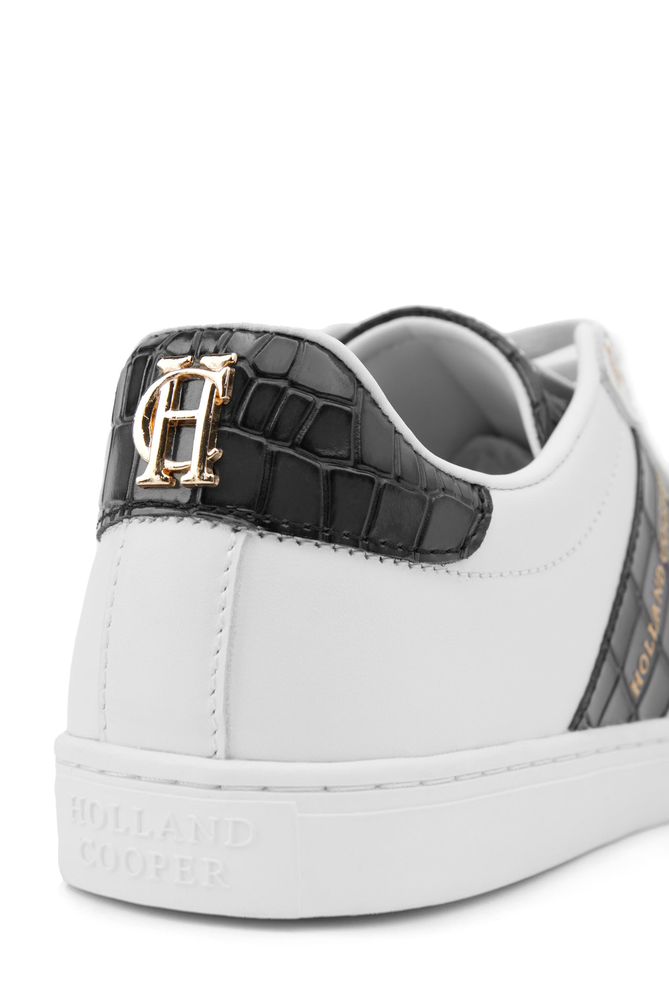 Close up of the back heel of a white leather trainer detailed with a diagonal stripe of black croc embossed leather with gold foil branding and a black croc embossed leather tongue and heel with gold hardware 
