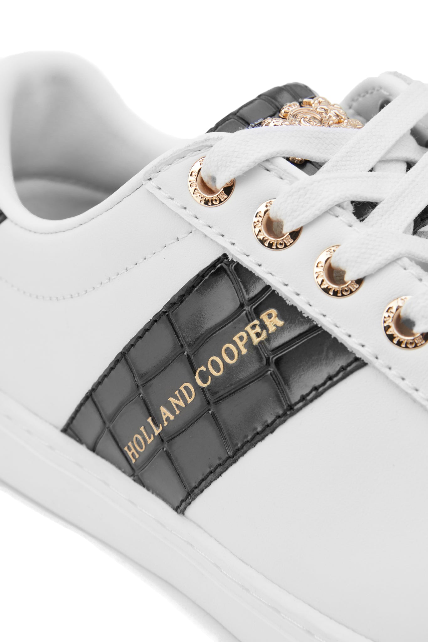 Close up of white leather trainer with white laces detailed with a diagonal stripe of black croc embossed leather with gold foil branding and a black croc embossed leather tongue and heel with gold hardware 
