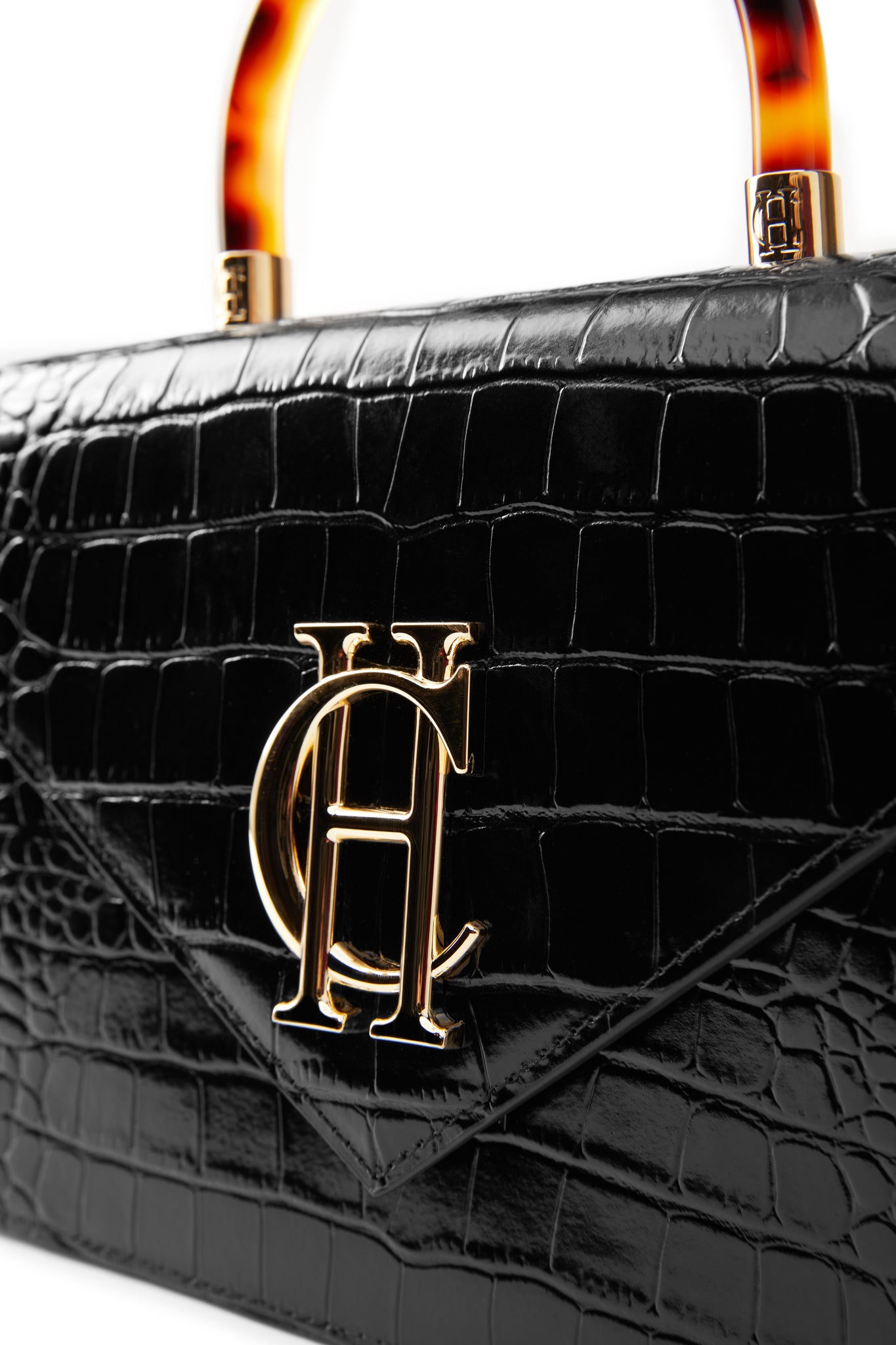 close up of gold hardware on the front of the black croc embossed leather shoulder bag with acetate tortoiseshell top handle