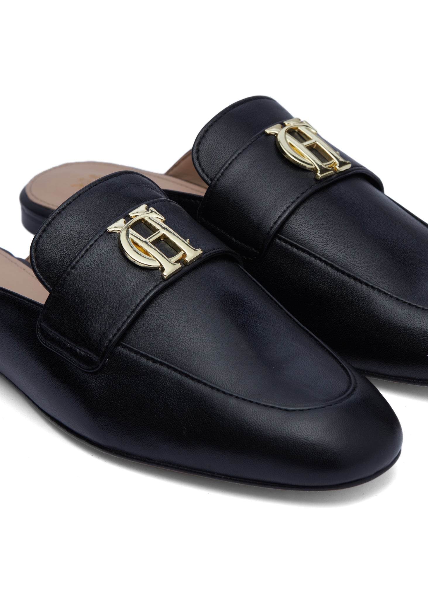 Close up of the gold hardware on black leather backless loafers with a slightly pointed toe 