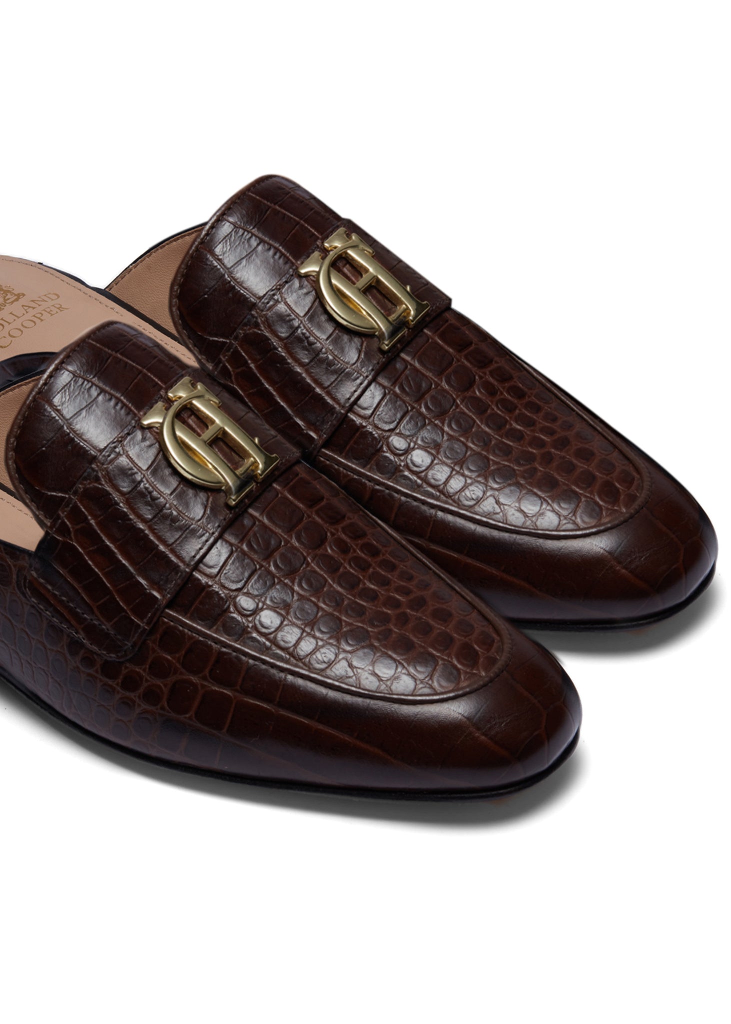 Close up of gold hardware brown croc embossed leather backless loafers with a slightly pointed toe and gold foil branding on the inner sole