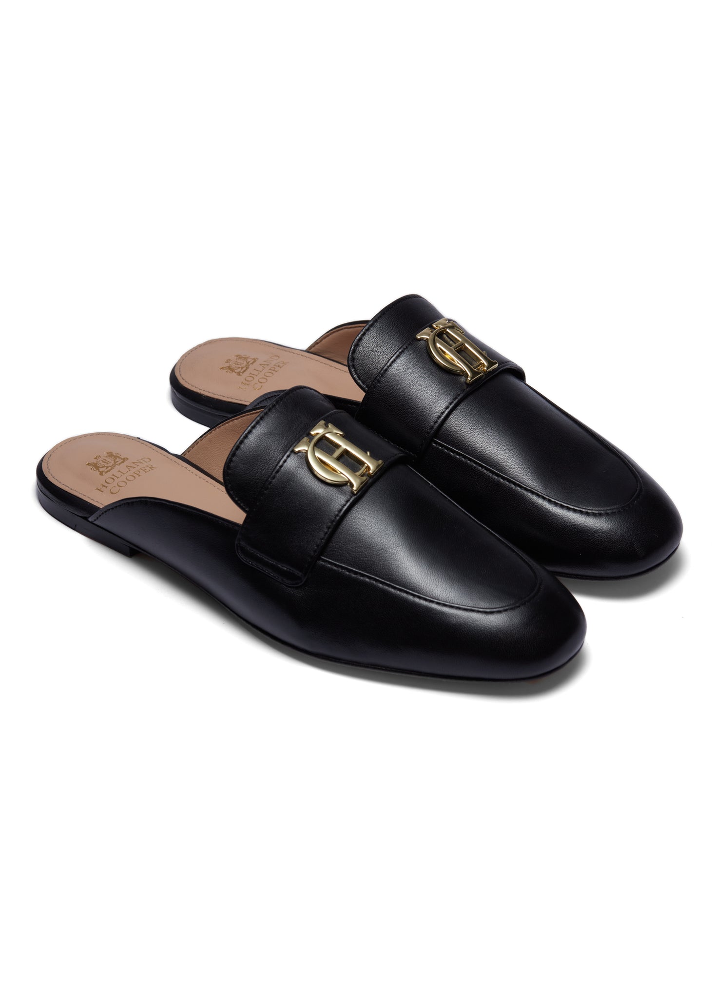 Side view of black leather backless loafers with a slightly pointed toe and gold hardware to the top with gold foil branding to the inner sole