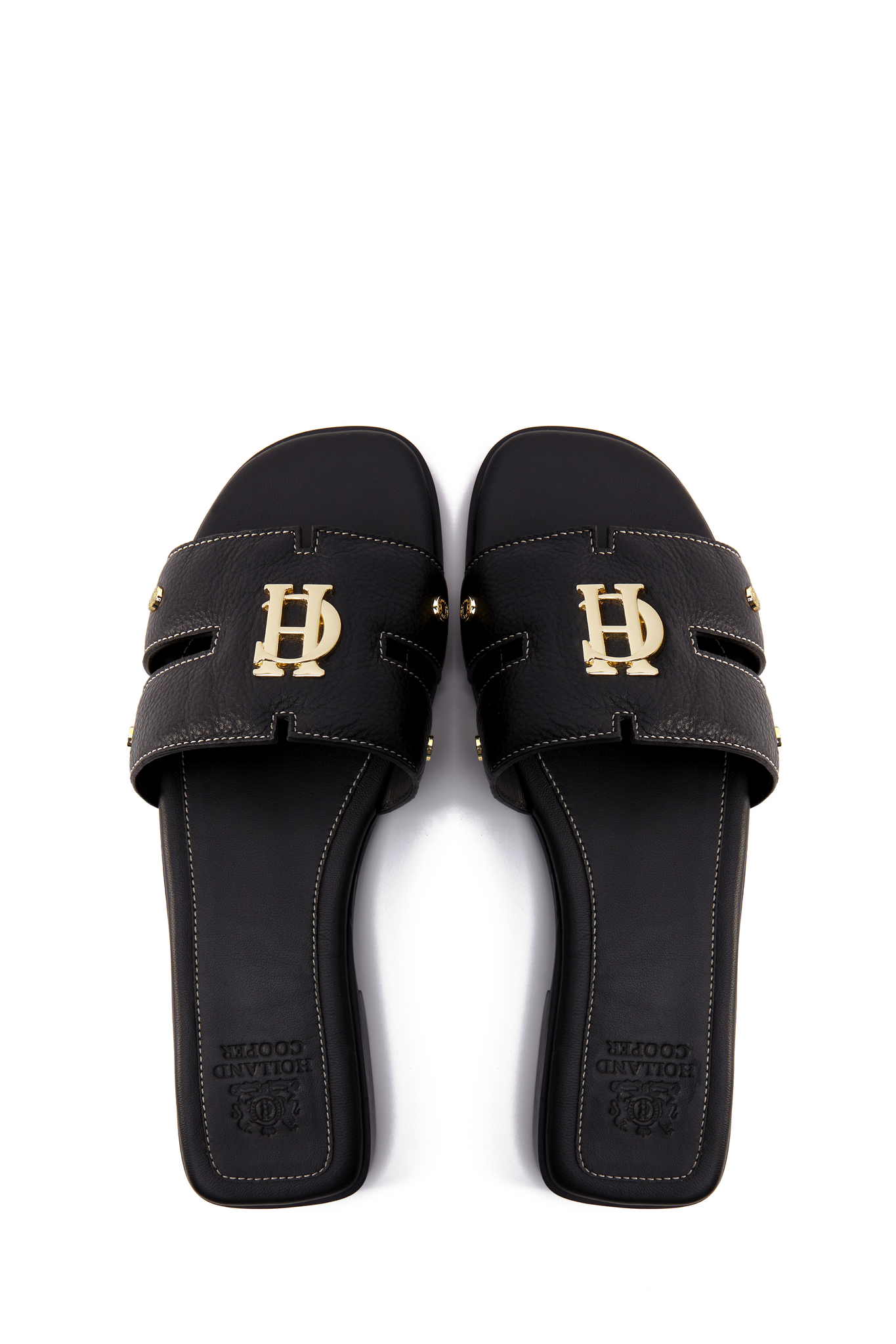 Birds eye view of black leather sliders with contrast white stitching, a black leather sole and gold hardware