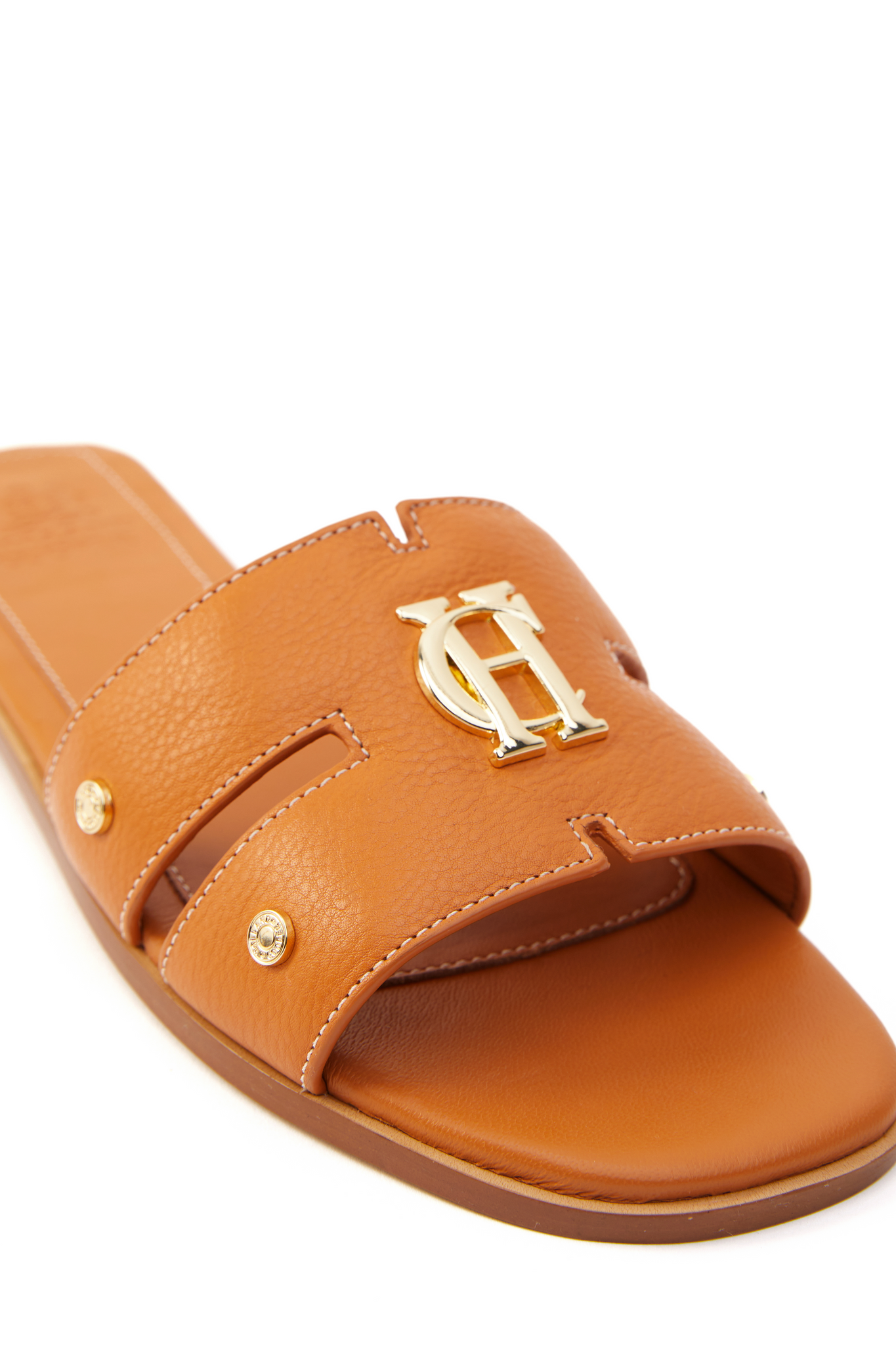 Close up of tan leather sliders with contrast white stitching, a tan leather sole and gold hardware