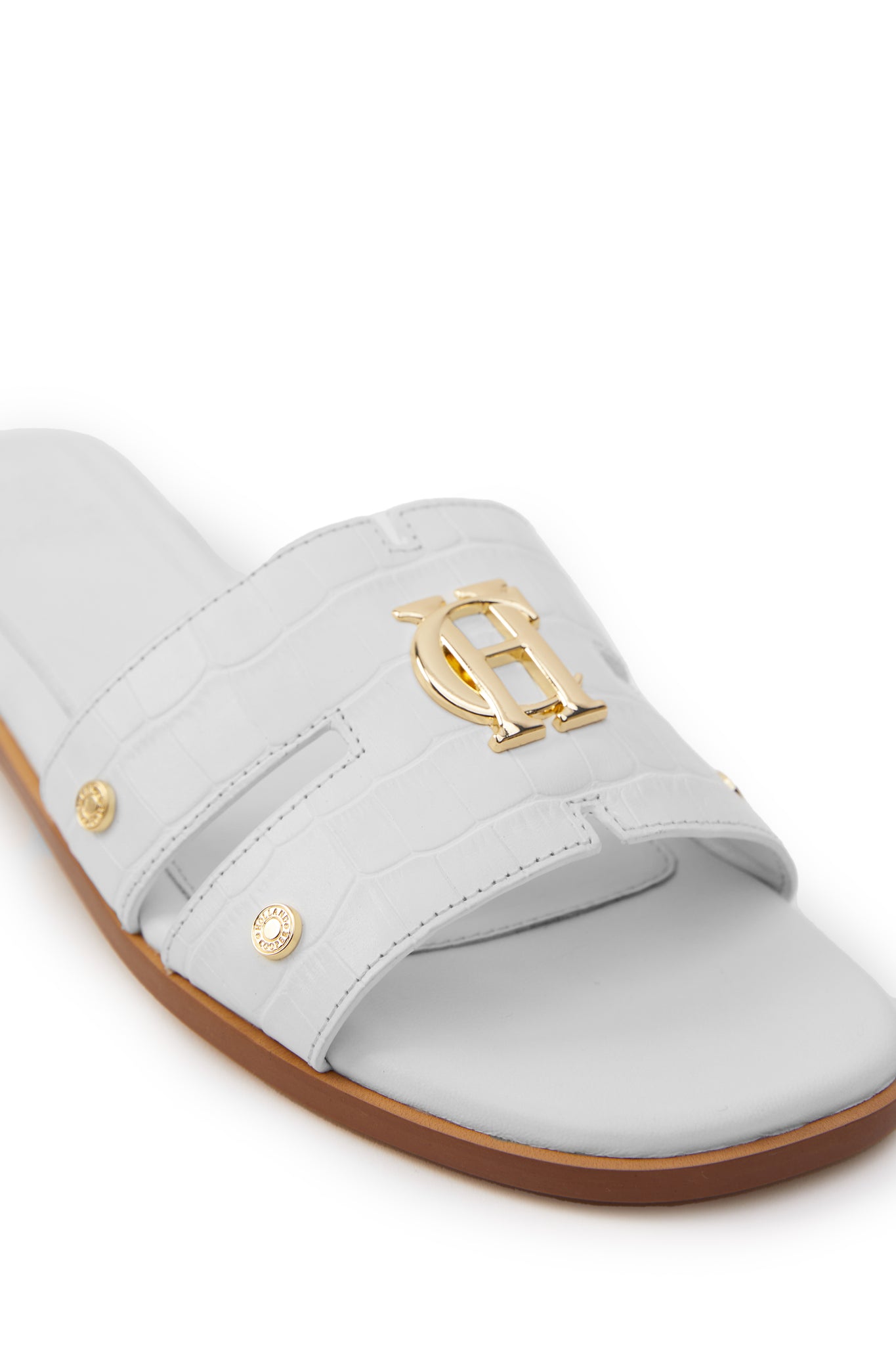 Close up of white croc embossed leather sliders with a tan leather sole and gold hardware